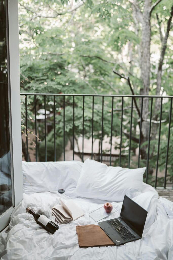 pexels-photo-4099388-4099388 Relaxing on a cozy balcony with a laptop and wine bottle, surrounded by lush greenery.